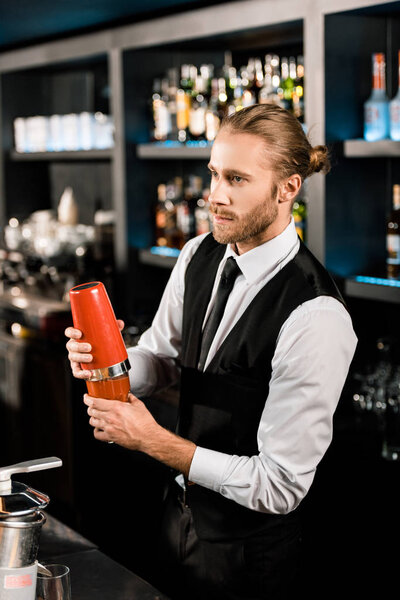 Handsome barman mixing cocktail in shaker 