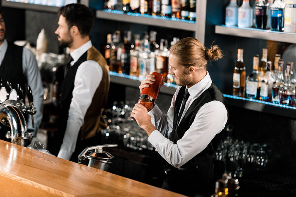 Barman mixing cocktail in shaker and standing in bar