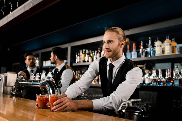 Handsome bartender serving drinks in glasses 