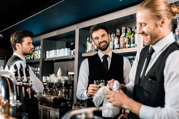 Handsome bartenders smiling in bar and cleaning glasses 