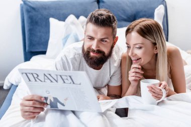 sakallı adam ve genç kadın yatakta yatan ve seyahat gazete okuma kahve fincanı ile