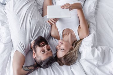 yatakta yatan ve birbirine bakarak dijital tablet ile genç çift