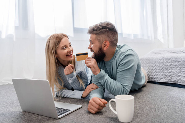 Smiling couple lying on floor with laptop and credit card