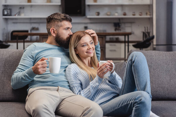 Husband kissing head of wife and sitting on sofa 