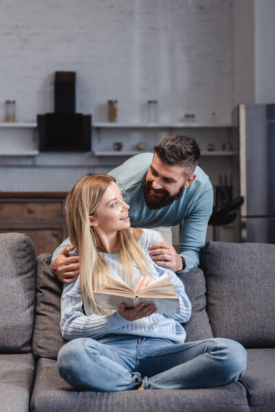 Husband hugging cheerful wife with book 