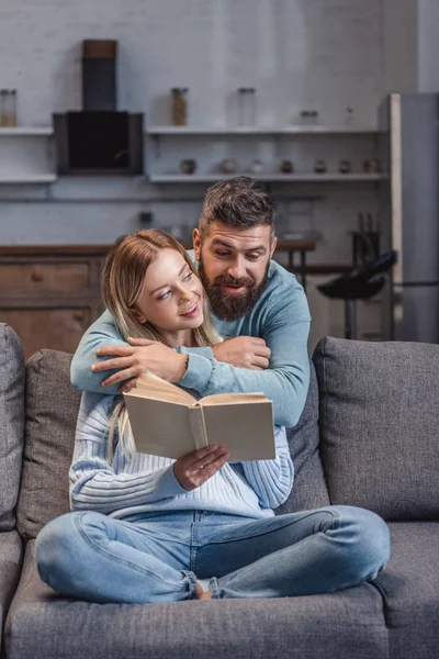 Fröhlicher Ehemann Umarmt Schöne Frau Mit Buch — Stockfoto