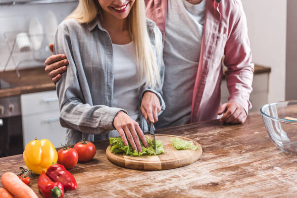Cropped view of couple preparing salad in kitchen 