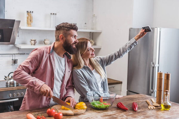 Cheerful couple taking selfie on smartphone in kitchen 