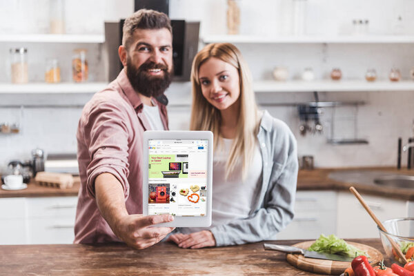 couple holding digital tablet with ebay app on screen at kitchen
