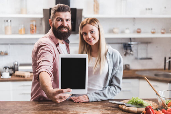 couple holding digital tablet with blank screen while cooking breakfast