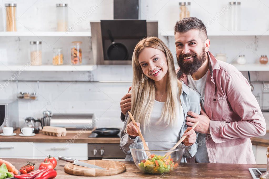 smiling couple hugging while cooking dinner at kitchen