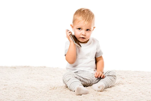 愛らしい幼児少年スマート フォンを押しながら白で隔離のカーペットの上に座って — ストック写真