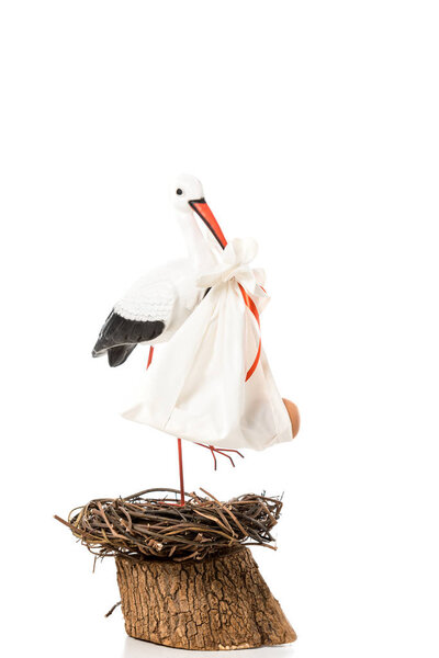 decorative stork holding in beak baby nappy and standing in wicker nest isolated on white