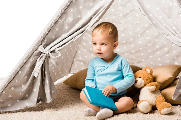 ブルーブックを押し枕と白で隔離テディベア ウィグワムに座っている幼児の少年 — ストック写真