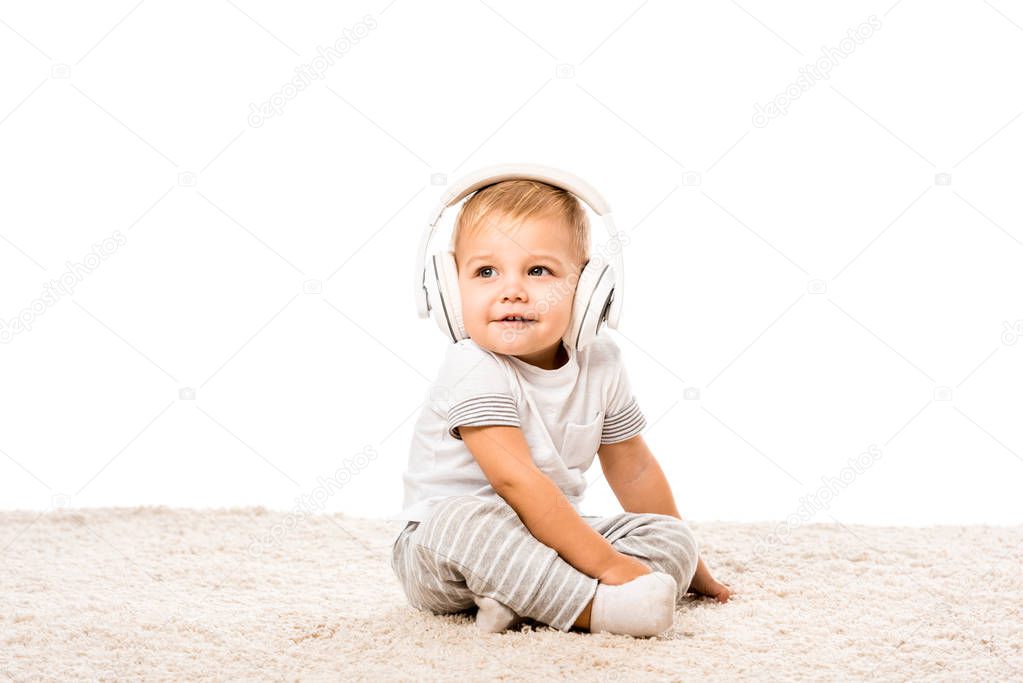 toddler boy sitting on carpet with headphones isolated on white