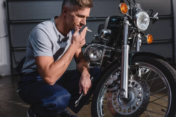 Bonito Adulto Mecânico Fumar Segurando Chave Enquanto Fixa Motocicleta Garagem — Fotografia de Stock Grátis