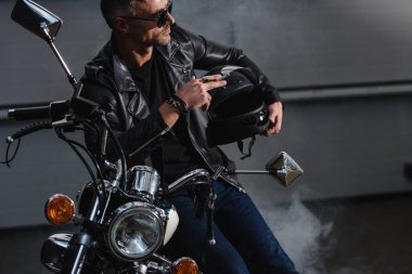motosiklet garaj ve Sigara İçilmeyen tarafından ayakta güneş gözlüğü yakışıklı bisikletçinin