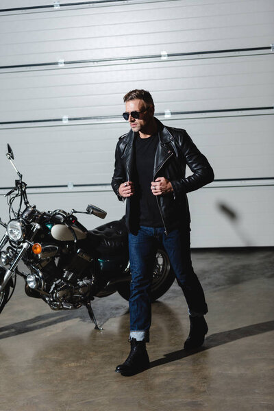 cool guy in sunglasses and leather jacket walking in garage