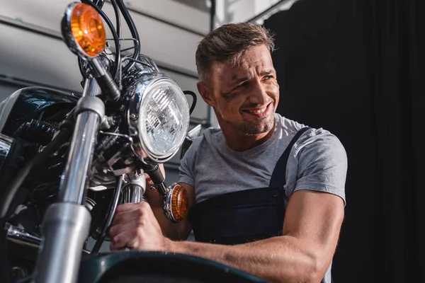 微笑的机械师检查摩托车前轮在车库 — 图库照片