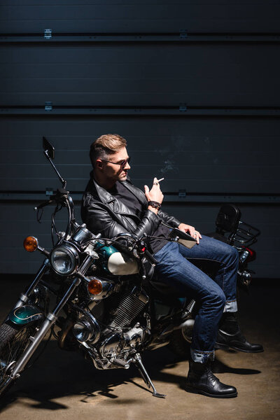 handsome guy in sunglasses leaning on motorcycle in garage