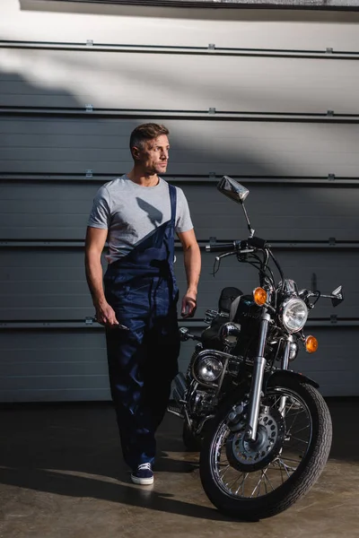 大人のメカニック ガレージでバイクの近くに立ってのオーバー オールの — ストック写真