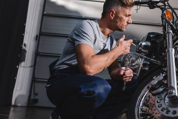 mechanic checking motorcycle front wheel and smoking in garage