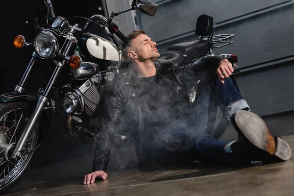 英俊的男人在皮夹克休息摩托车在车库 — 免费的图库照片