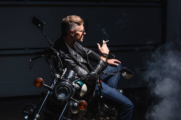 handsome biker in sunglasses sitting on motorbike in garage