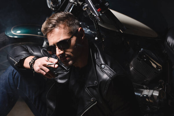 handsome guy in sunglasses sitting by motorcycle in garage