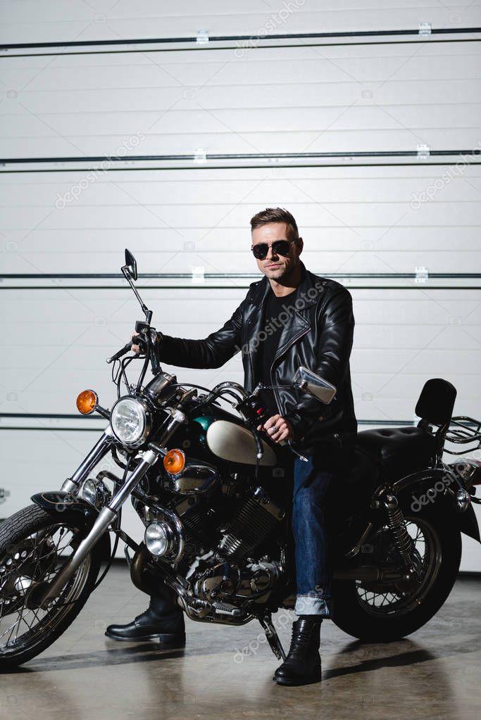 handsome man in sunglasses sitting on motorcycle and looking at camera