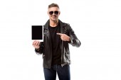 Lächelnder Mann in Lederjacke zeigt mit dem Finger auf digitales Tablet mit leerem Bildschirm auf weißem Hintergrund