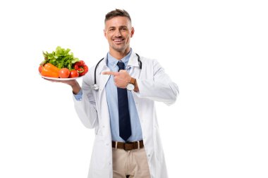 tabak taze sebze ve izole beyaz, sağlıklı beslenme kavramı üzerinde yeşil parmak ile işaret eden doktor gülümseyen