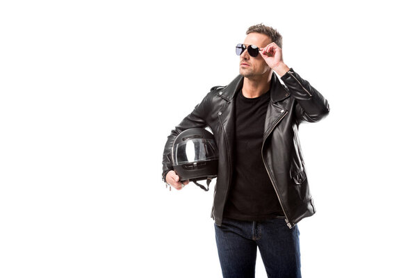 man in leather jacket and sunglasses holding motorcycle helmet and posing isolated on white