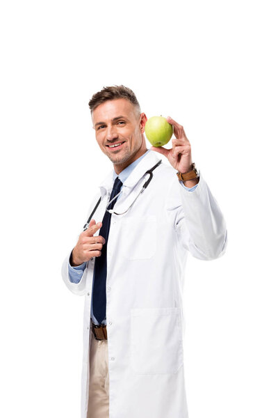 smiling doctor pointing with finger at green apple isolated on white, healthy eating concept