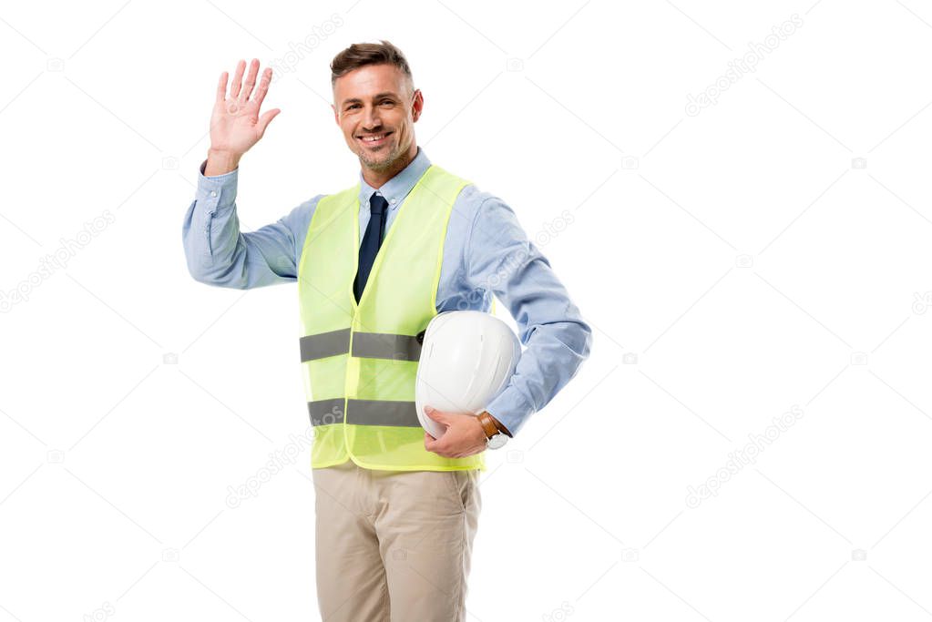 smiling engineer holding helmet, waving and looking at camera isolated on white