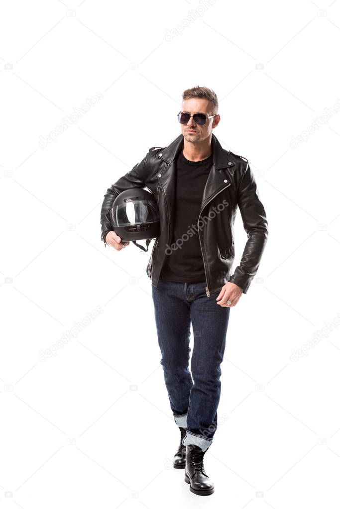 confident man in leather jacket and sunglasses holding motorcycle helmet isolated on white