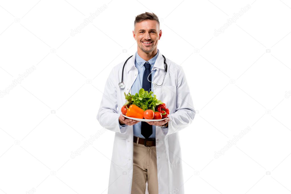 doctor looking at camera and holding plate of fresh vegetables isolated on white, healthy eating concept