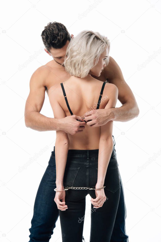 man unzipping bra of handcuffed blonde woman from behind isolated on white