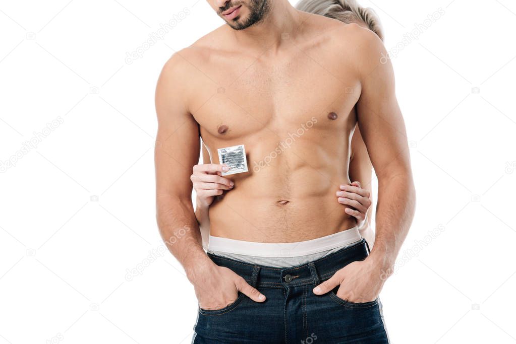 partial view of woman hugging shirtless man from behind and holding condom isolated on white, safe sex concept