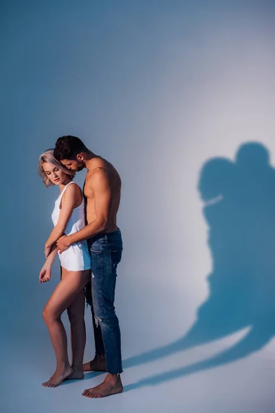 shirtless man hugging woman from behind with shadows on dark blue background