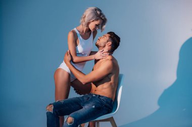 güzel genç kadın koyu mavi arka plan ile sandalye üzerinde oturan adam tutkuyla bakarak