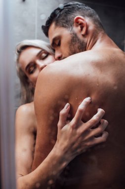 selective focus of passionate naked heterosexual couple hugging and kissing while taking shower together clipart
