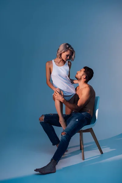 上半身裸の男が椅子に座っていると暗い青色の背景の美しい女性を見て — ストック写真