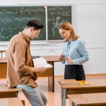 Студент мужского пола держит книгу рядом с учительницей в классе