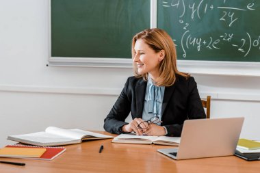 Dizüstü bilgisayar ve kitap yakın masada oturan kadın öğretim üyesi 