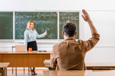 Seçici odak masada oturan ve el yükselterek erkek öğrenci
