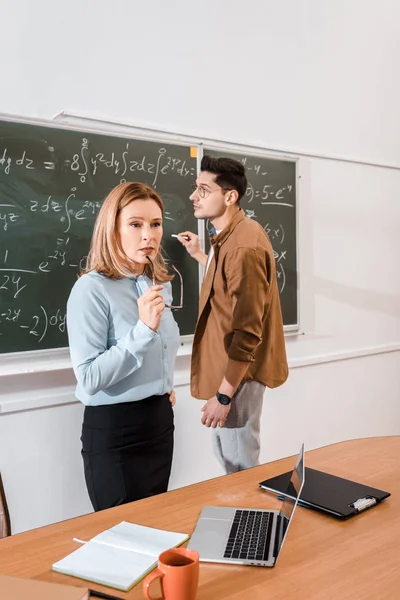 Nauczyciel Myślenia Ręku Trzyma Okulary Student Stojący Pobliżu Chalkboard — Darmowe zdjęcie stockowe