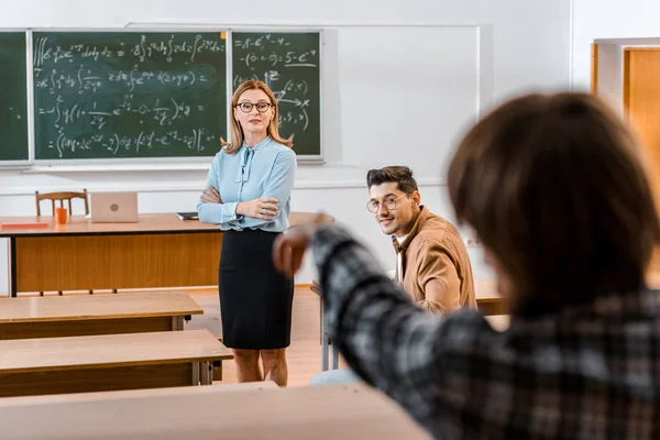 女教师讲解教材的选择性焦点 而男学生看同学 — 免费的图库照片