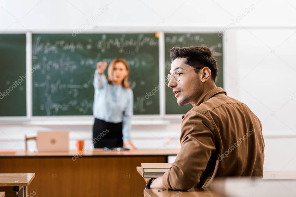 Selective focus of young student sitting in classroom with teacher on background 