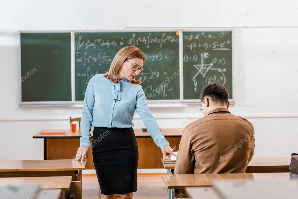 selective focus of female teacher and male student during exam in classroom